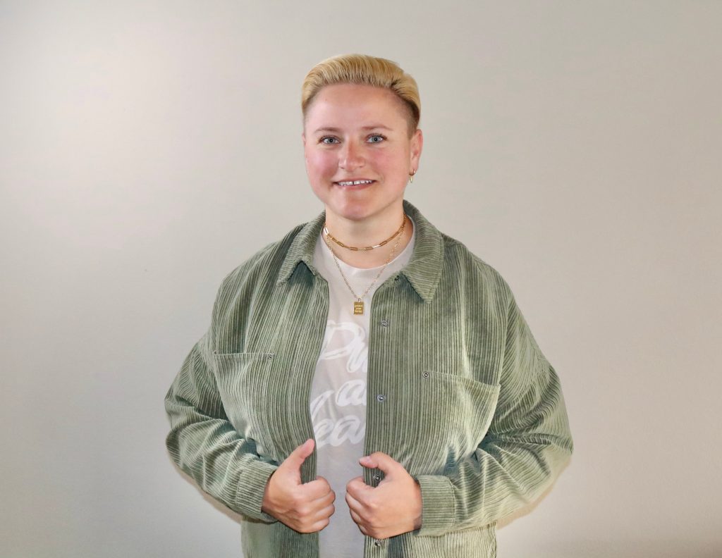 Coach Bea Schwaiger lächelt in die Kamera, hinter ihr eine braune Wand.