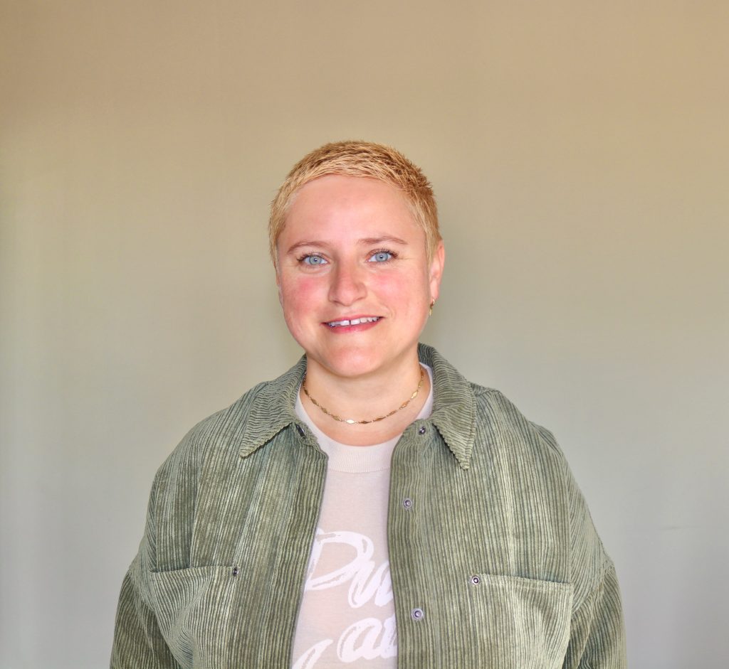 Coach Bea Schwaiger lächelt in die Kamera, hinter ihr eine braune Wand.